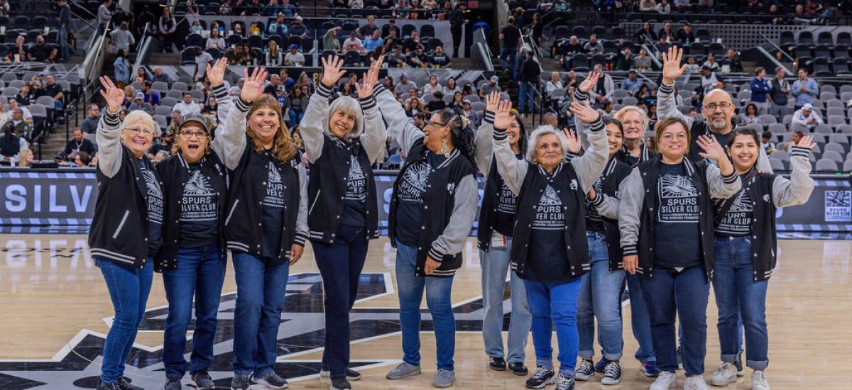 Group of Spurs Silver Club members waving and smiling on the San Antonio Spurs basketball court during a game.